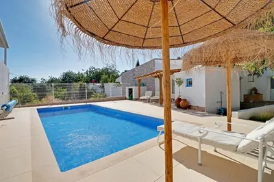 a swimming pool with an umbrella and chairs and a house at Casa Pedra São Romão in São Brás de Alportel