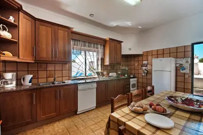 a kitchen with wooden cabinets and a table with a bowl of fruit at Villa Terra by Villa Plus in Albufeira