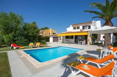 a swimming pool with chairs and an umbrella and a house at Villa Tupi by Villa Plus in Boliqueime