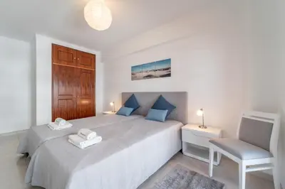 a white bedroom with a large bed and a chair at Quarteira Beach - 2 D by HelloVacations in Loulé