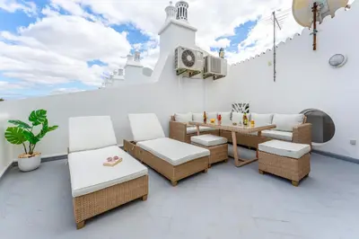 a patio with a table and chairs and a clock on a building at Casa Perola - Vale do Garrão in Almancil