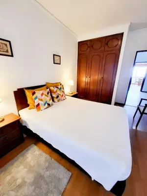 a bedroom with a large white bed and a wooden cabinet at T2-MAMAMIA II Frente Mar in Quarteira