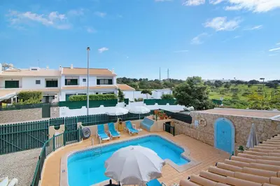 a swimming pool with an umbrella and chairs and a building at Villa Catarina in Albufeira