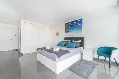 a white bedroom with a bed and a blue chair at Villa das Amendoeiras by HelloVacations in Albufeira