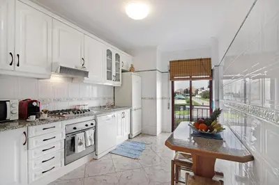 a kitchen with white cabinets and a table with a bowl of fruit at Columbus Beach Apartment in Quarteira