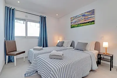 two beds in a white room with blue curtains at Ocean Chic by the Beach in Albufeira