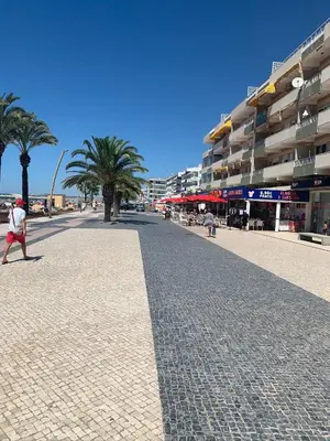 a man walking down a street with palm trees and buildings at Eine Wohnung für den perfekten Urlaub !!! in Quarteira