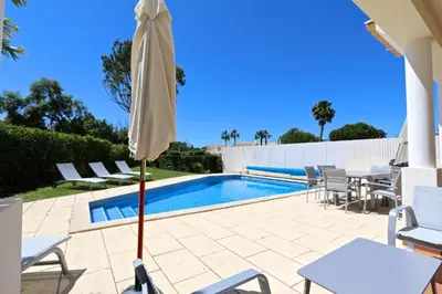 a patio with an umbrella and chairs and a pool at Spacious Vilamoura Villa 4 Bedrooms Villa Amendoeira Table Tennis in Quarteira
