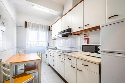 a kitchen with white cabinets and a table and a refrigerator at BeGuest Santa Eulália Apartment in Albufeira