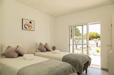 two beds in a white room with a window at O Pinhal do Avô - BY BEDZY in Almancil