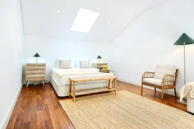 a white bedroom with a bed and a chair at Zen & Tan Apartment in Faro