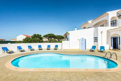 a swimming pool with blue chairs and a building at Villa Dois Pinheiros in Albufeira