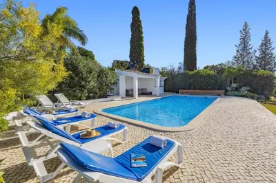 a swimming pool with blue and white chairs and a house at Villa Casa do Amendoal by Villa Plus in Albufeira