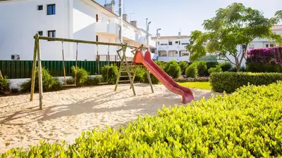 a playground with a swing in a garden at Central Albufeira 2-B Apt Sleeps 6 Pool Parking in Areias Sao Joao