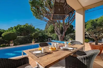 a wooden table with food on a patio next to a pool at Villa Anna - Vale de Lobo in Faro