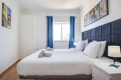 a bedroom with a large white bed with blue curtains at Old Town 2BR 50m Ocean w/ AC Wi-Fi Parking Terrace in Albufeira