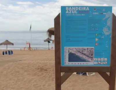 a sign on a beach with the ocean in the background at Seaside Serenity: 1BR with Breathtaking Ocean View in Quarteira