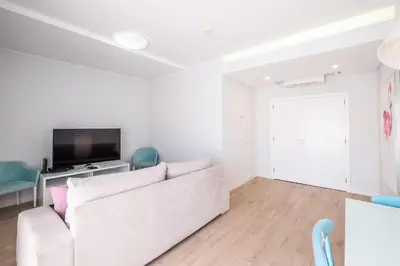 a white living room with a white couch and a tv at Al Marina View Uma - Lux apartment on the marina in Páteo