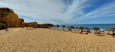 a beach with umbrellas and people sitting on the sand at Baia Village - Galé - Albufeira in Albufeira
