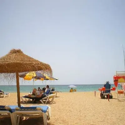a group of people sitting under an umbrella on a beach at Casa Dos Reis - Albufeira, Center in Albufeira
