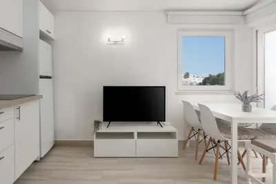 a white living room with a television on a white table at Sunny Albufeira - 5min to the beach by LovelyStay in Albufeira