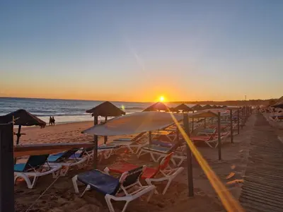 a beach with chairs and umbrellas at sunset at Appart Oura Strip in Albufeira
