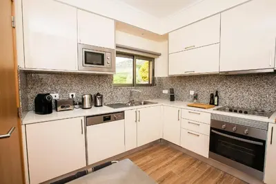 a kitchen with white cabinets and a sink and a microwave at Jardins da Marina Albufeira in Albufeira