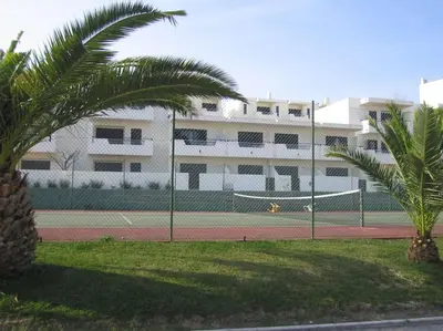 a tennis court with two palm trees in front of a building at Studio with great sea view, near the beach, with AC and pools in Albufeira